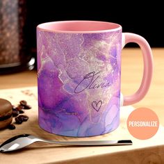 a pink and purple coffee mug sitting on top of a table next to a cookie