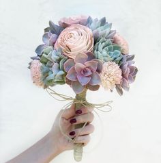 a woman's hand holding a bouquet of flowers with pink and green succulents