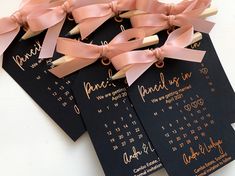 four black and gold wedding programs with pink ribbon tied around the front, on a white table