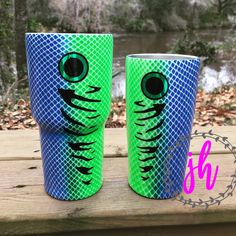 two green and blue cups sitting on top of a wooden table next to each other