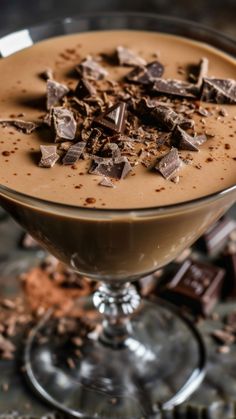 a chocolate dessert in a glass on a table with pieces of chocolate scattered around it