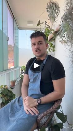 a man sitting in a chair next to a potted plant and wearing an apron