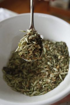 a spoon full of green tea is being held up by someone's hand over a white bowl