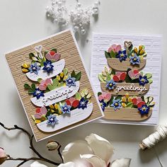 two cards with flowers on them sitting next to a flower pot and bead necklace