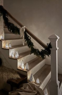 some lights are hanging on the banisters in front of a stair case that is decorated with garland and pine cones