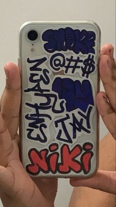 someone holding up their cell phone with graffiti on the back and bottom part of it