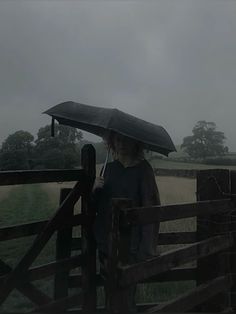 a woman holding an umbrella over her head while standing in front of a wooden fence