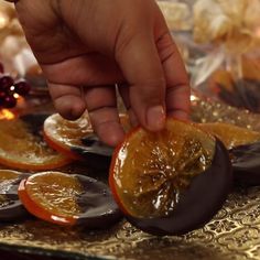 a person is peeling an orange slice on a tray with other fruit in the background