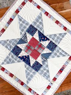 a quilted table topper with red, white and blue designs on it sitting on a wooden surface