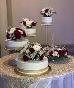 three tiered white wedding cake with red and white flowers on the top, sitting on a table