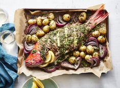 a fish covered in herbs and potatoes on a tray next to some lemon wedges