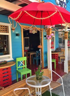 the outside of a restaurant with colorful tables and chairs under an umbrella on the patio