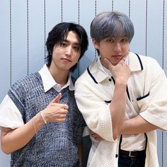 two young men standing next to each other in front of a wall with blue stripes