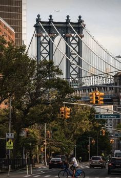 a man riding a bike across a street in front of a bridge and traffic lights