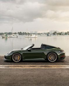 a green sports car parked on the side of a road next to a body of water