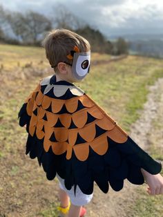 a young boy wearing a bird costume on the side of a dirt road with grass and trees in the background