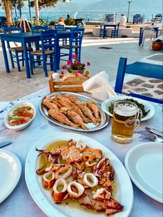 an outdoor dining area with plates of food and drinks on the table, overlooking the ocean