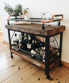 a bar cart with bottles and glasses on it sitting in front of a wall next to a potted plant