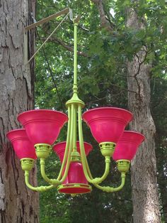 a green chandelier hanging from a tree in the woods with pink glass shades