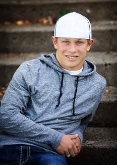 a young man sitting on the steps wearing a white hat and smiling at the camera