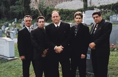 four men in suits standing next to each other at a cemetery with headscarves on