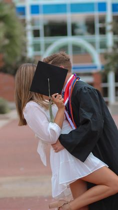 a young man and woman kissing each other in front of a building with a graduate's cap on