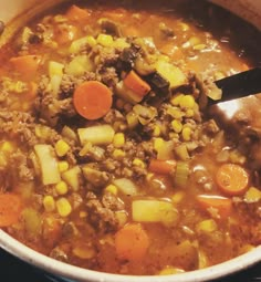 a pot full of soup with carrots, corn and meat on the stove top