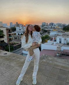 a woman holding a small child on top of a roof with the sun setting in the background