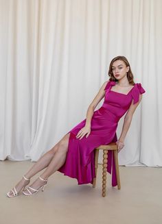 a woman in a pink dress is sitting on a chair and posing for the camera