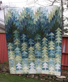 a quilted wall hanging in front of a red building with trees on it's side