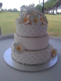 a three tiered wedding cake with flowers on the top is sitting on a table