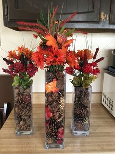 three vases filled with flowers and pine cones on top of a wooden countertop