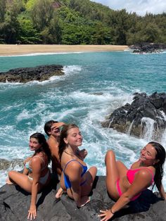 four women in bikinis sitting on rocks near the ocean