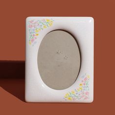 a white square object with flowers painted on the side and an oval hole in the middle