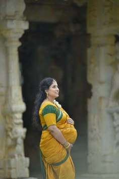 a woman in a yellow and green sari standing next to an old stone structure