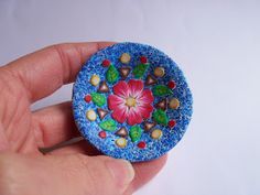 a hand holding a small blue brooch with flowers on it