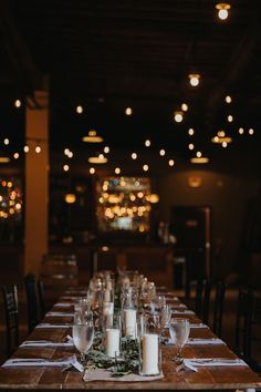 a long table with candles and place settings on it in a dimly lit dining room