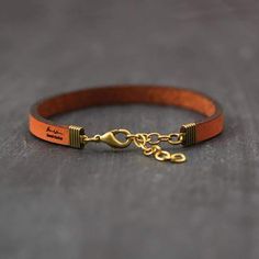 an orange leather bracelet with gold chain and clasps on the end, sitting on a gray surface