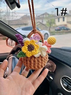 a hand holding a small crocheted flower basket hanging from the dashboard of a car