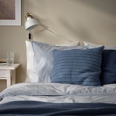 a bed with blue and white pillows on top of it next to a night stand