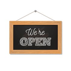 we're open sign hanging on a wooden frame with chalkboard lettering in the background