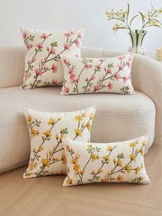 three pillows sitting on top of a couch next to a vase with flowers in it