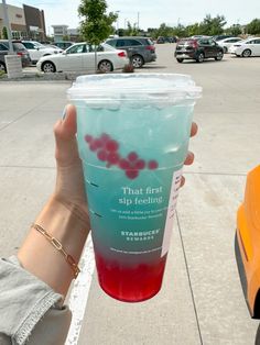 a person holding up a cup with liquid on it in a parking lot next to parked cars