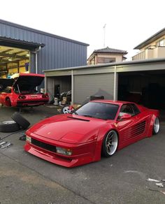 a red sports car parked in front of a garage with two other cars behind it