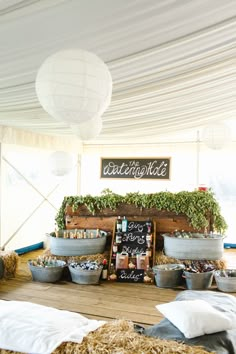 an outdoor event with hay and plants in buckets on the floor next to a chalkboard sign