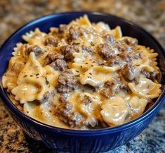 a blue bowl filled with pasta and meat covered in cheese sauce on top of a granite counter