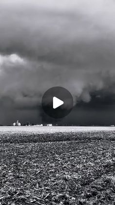 a black and white photo of a field with storm clouds in the sky behind it