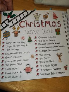 a christmas movie list on a wooden table with a hand holding a pen and pencil