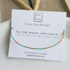 the beaded bracelet is on display in front of a card that says morse code bracelet to the moon and back