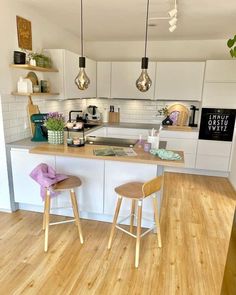 two stools are in the middle of a kitchen with white cabinets and wood floors